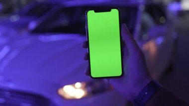 NEW YORK - 19 Nisan 2019: Gece şehir mavi ışıklı arka plan üzerinde dikey yeşil ekranlı akıllı telefon kullanan erkek eli beyaz araba iletişimi cihazı dijital cihaz mobil dokunmatik mobil yavaş çekim