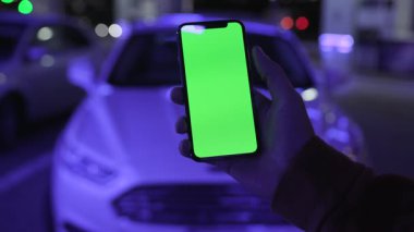 NEW YORK - 19 Nisan 2019: Gece şehir mavi ışıklı arka plan üzerinde dikey yeşil ekranlı akıllı telefonu kullanarak dijital cihaz, mobil dokunmatik telefon, yavaş çekim