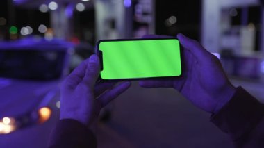 NEW YORK - 19 Nisan 2019: Renkli mavi ışıklı adam elinde yatay yeşil ekranlı akıllı telefon kullanıyor beyaz araba iletişimi cihazı dijital cihaz telefon dokunmatik mobil yavaş çekim