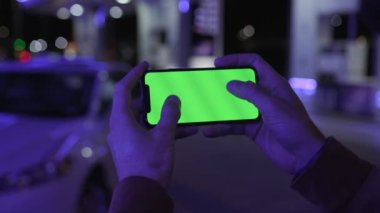 NEW YORK - 19 Nisan 2019: Gece şehir mavi ışıklı arka plan üzerinde yatay yeşil ekranlı akıllı telefon kullanan erkek eli beyaz araba iletişimi cihazı dijital cihaz mobil dokunmatik mobil yavaş çekim