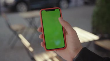 NEW YORK - 5 Nisan 2018: Akıllı telefonun maket yeşil ekranla dikey pozisyonda gösterilmesi. Genç sosyal iş adamı açık kafede dinlenirken internetten haber okuyor..