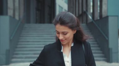 Çekici beyaz iş kadını modern ofis binasının yanında yürüyor telefon görüşmelerine cevap veriyor arkadaşça sohbetler ediyor neşeyle gülümsüyor..