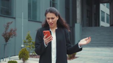 Kafkasyalı güzel bir kadın akıllı telefondan olumsuz geri bildirim alıyor. Karışık kollu, açık ofis binasının yanında sürpriz bir şekilde duruyor..