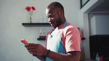 Kaçak Afro-Amerikalı adam internette harika haberler okuyor ve anında başarı sayesinde gülümsüyor. Mutfakta yemek önlüğü giymiş mutlu, şaşırmış adam..