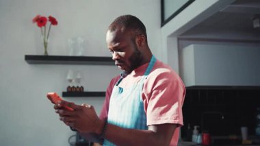 Neşeli siyah yakışıklı adam akıllı telefondan beklenmedik haberler alıyor, zaferin yumruğunu sıkıyor, mutfakta başarısını kutluyor..