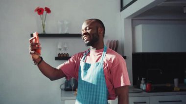 Video görüşmesi için akıllı telefonu kullanan, arkadaşlarıyla internetten sohbet eden, kendi mutfağında kalan yakışıklı bir zenci. Bağlantı. İletişim kuran insanlar.