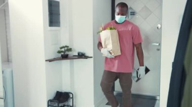 Kendini işine adamış bir insan koruyucu eldiven ve maske takıp bir evin girişinde alışveriş yapar.