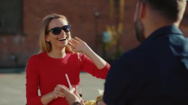 Kokteyl içen genç bir adam ve bir kadın sokak kafesinde hamburger yiyorlar. Birlikte yemek yiyorlar. Kız arkadaşlarıyla yemek yiyorlar.