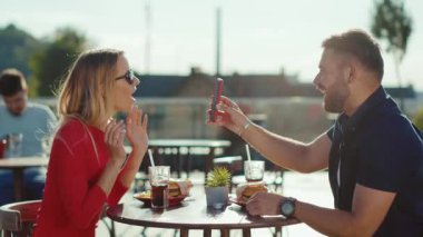 Mutlu genç adam ve kadın kokteyl içerken hamburger yerken sokak kafesinde telefon kullanırken yemek yerken kız arkadaş yemek yerken neşeli ağır çekimde portre çekerken.