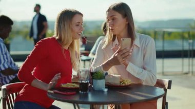İki genç kadın dinleniyor. Yaz Kafe Caddesi Kardeşler Kafesi 'nde telefon kokteyli içiyorlar. Şehir arkadaşlığı modelleri yavaş çekimde.
