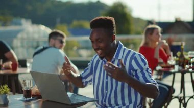 Bir kafede oturan Afrikalı Amerikalı yüksek sesle arka planda bir dizüstü bilgisayar kullanıyor insanlar onunla tartışıyor ve çok ırklı, yavaş çekimde, yavaşça konuşmak istiyorlar.
