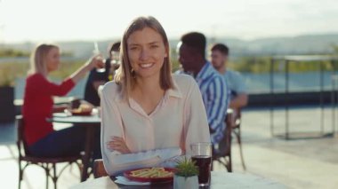 Gülücükler saçan, güzel, güzel bir kadın, gün ışığında kafede kameraya bakıyor. Günlük yaşam tarzı, rahatlık, kendine güvenen genç, yavaş çekim.