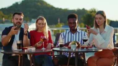 Şirket arkadaşları sokak kafesinde oturup içiyor. Akıllı telefonlar kullanıyor. Şehir manzarası gülümsüyor.