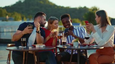 NEW YORK - 5 Nisan 2020: Gülümseyen şirket arkadaşları sokak kafeteryasında oturmuş içiyor, akıllı telefonlar kullanıyor, haftasonu kentsel tatil partisi arkadaşlığı etkinliği yavaş çekim