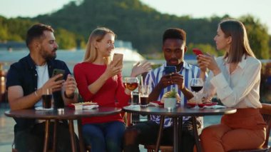 NEW YORK - 5 Nisan 2020: Mutlu şirket arkadaşları sokak kafesinde oturup içiyor, akıllı telefonlar kullanıyor, haftasonu şehir merkezinde tatil arkadaşlığı etkinliği yavaş çekim