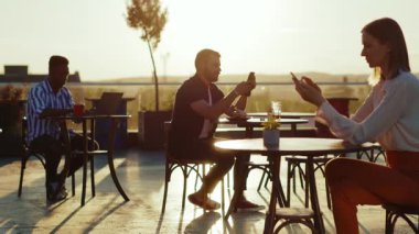 Kafede oturan insanlar, Sunlight Caddesi Restoranı 'nda telefon kullanıyor. Turistik tatil gezileri için gösteri yeri masasında çalışıyorlar. Yavaş çekimde içki içiyorlar.