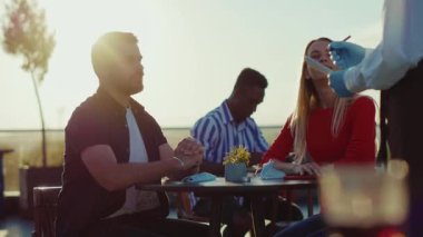 Gün ışığında mutlu genç bir çift parkın dışındaki masada oturmuş yemek siparişi veriyor. Yemek siparişi veriyor. Hafta sonları çalışan adam kafenin önünde perakende satış siparişi satıyor.