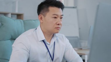 Şok olmuş Asyalı işadamı stresli hissediyor, bilgisayar ekranına bakıyor, problem için endişeleniyor. Genç erkek kötü internet haberleri okuyor. Ofis masasında oturuyor..