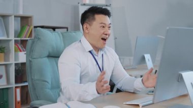 Mutlu Asyalı genç işadamı bilgisayar ekranına bakıyor, ya duygu kazananı ya da kazananı. Erkek oyun oynadığını sevinçle haykırıyor. Heyecanlı, sevinçli, kutlama başarısı.