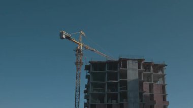 Yeni inşaat alanının insansız hava görüntüleri. Tamamlanmamış konut binasının üstündeki yüksek kule vinci. Gündüz vakti. Mavi gökyüzü. Şehir manzarası.