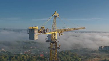 Vinç kulesinin etrafında insansız hava aracı uçuşları. Yüksek endüstriyel vinç kaldırma makineleri ve tamamlanmamış binalar. Şehir emlak binası.