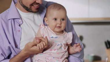 Sakallı yakışıklı bir babanın, güzel bir kızı ellerinde tuttuğu bir görüntü. Modern mutfağın bulanık arka planında kameraya bakan komik çocuğun yakın plan görüntüsü. Kapalı
