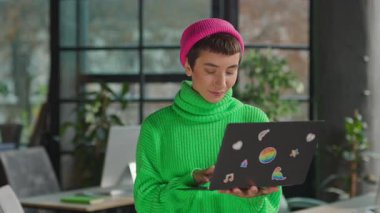 Elinde gökkuşağı çıkartmalarıyla kameraya bakan gülümseyen eşcinsel kadın.