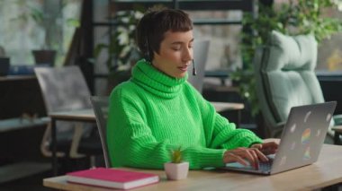 Diz üstü bilgisayarda oturan ve çağrı merkezinde mikrofon başında konuşan transseksüel kişi.