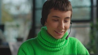 Çağrı merkezinde çalışırken mikrofon kullanan, kulaklıkla gülümseyen eşcinsel kadın.