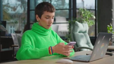 Açık yeşil kazaklı düşünceli transseksüel kadın akıllı telefonda sohbet ediyor.