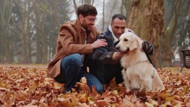 Sonbahar parkında yürürken birkaç kültürlü adamın beyaz köpeği okşaması.