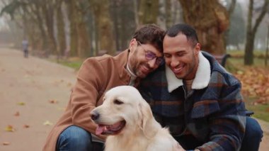 Neşeli, çok ırklı eşcinsel çift parkta yürürken köpeğini okşuyor.