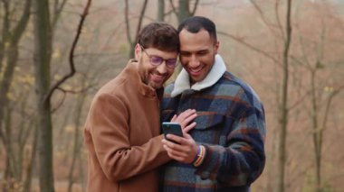 Aşıkken gülen iki duygusal eşcinsel sonbahar parkında akıllı telefon ekranına bakıyor.