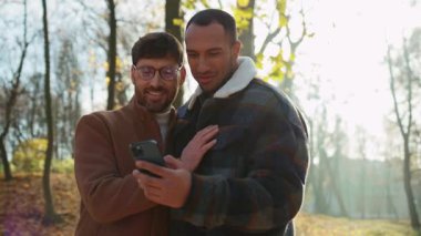 Akıllı telefon kullanan iki sakallı adamın neşeli, çok ırklı genç görüntüsü.