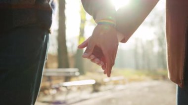 Güz parkının bulanık arka planında gökkuşağı bileziğinde el ele tutuşan eşcinsel çift