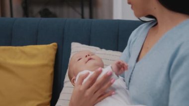 Yeni doğmuş bir bebeği kucağında tutan ve modern bir dairede gülümseyen genç bir anne. Çocukluk. Annelik. Yavaş çekim