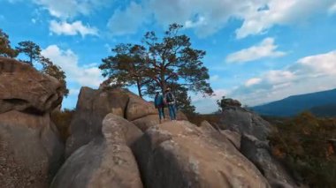 Hava FPV helikopter görüntüsü, kayalıkların seyahat rotasını gösteriyor. Maceraperest erkek kadın turistler büyük taşlara tırmanıp tırmanıyorlar..