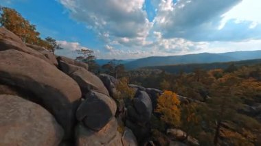 Güzel doğa. Sonbahar manzarasında muhteşem kayaların FPV insansız hava aracı görüntüleri. Yürüyüş yolu. Uçuruma tırmanan bir çift genç yürüyüşçü..