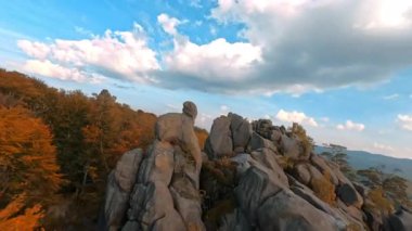 Sinema doğasında havadan FPV uçuş görüntüleri. Rengarenk sonbahar ormanları arasında muhteşem, vahşi, kayalık bir dağ. Hippi turist dağın tepesinde kollarını kaldırıyor. Yürüyüş.