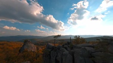 Vahşi kayaların, pitoresk ormanın ve doğa ufuk çizgisi manzarasının sinematik FPV helikopter görüntüsü. Dağlarda zıplayan hippi yürüyüşçüler. Manevra yapılabilir uçuş.