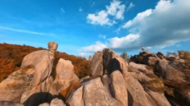Güzel sonbahar doğasının hava yolculuğu görüntüleri. Pürüzsüz büyük taş kayalar ve vahşi ağaçlar. Hippi adam dağın tepesinde aşırı atlıyor..