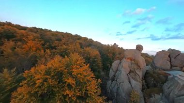 Taştan kayalar, renkli sonbahar ormanı ve mavi gökyüzü olan sinematik dağların ilham verici FPV görüntüleri. Doğa manzarası. Seyahat hedefi.