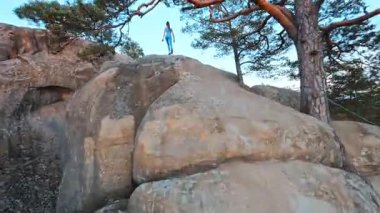 FPV hava aracı, genç fitness kızının dağın tepesinde jimnastik esneme egzersizleri yaptığını gösteriyor. Tırmanma aktivitesi. Yürüyüş. Dovbush Kayaları. Doğal manzara..