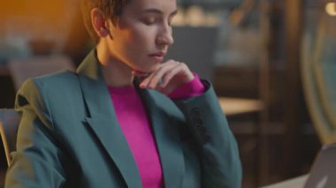 Pembe saçlı kendine güvenen genç bir kadın ofis gecesinde LGBT çıkartmalı dizüstü bilgisayar kullanıyor.