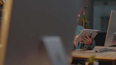 Ofisteki pembe saçlı kadın, geceleri LGBT çıkartmalı tablet bilgisayar kullanıyor.