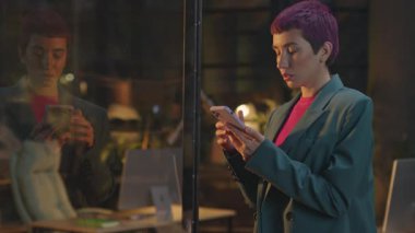 Pembe saçlı, yorgun ve üzgün genç bir kadın gece ofiste telefonla konuşuyor. LGBT