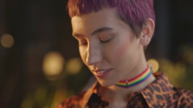 Pembe saçlı, boğazı düğümlenmiş gülümseyen kadın gece ofisindeki kameraya bakıyor.