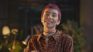 Pembe saçlı ve boğazı düğümlenmiş kadın ofiste gülümseyen kameraya bakıyor.