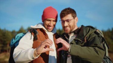 Gülümseyen çok ırklı genç eşcinsel çift spor giyim kuşamında kalp işareti yapıyor.