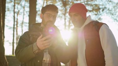 Spor elbiseli, gülümseyen iki erkek turist el ele tutuşup nehir kenarında yürüyorlar.